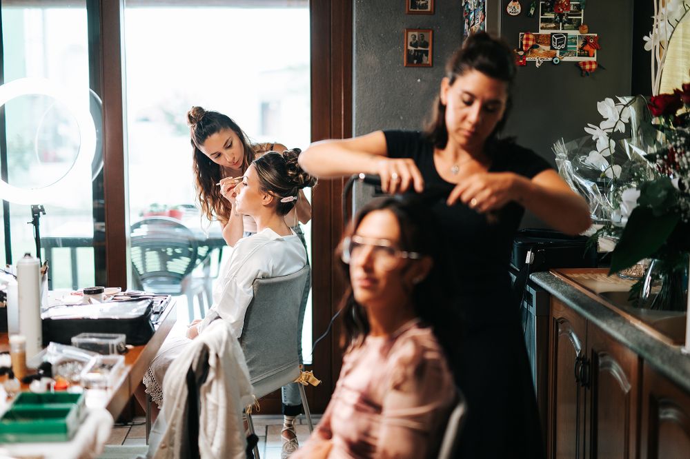 Professional hair and makeup artists preparing bride and bridesmaids for wedding ceremony indoors.