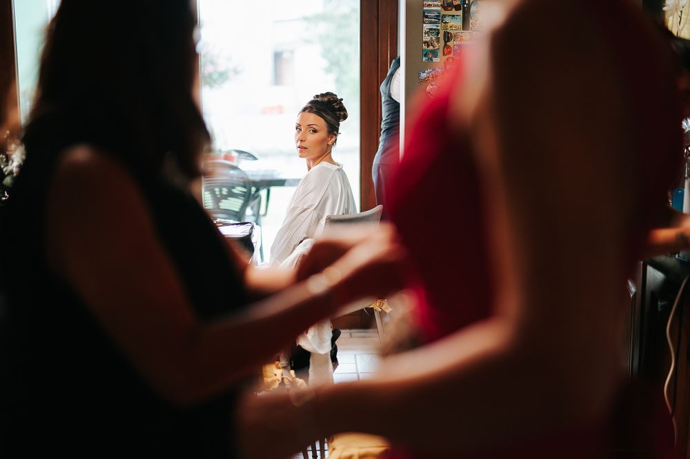 Beautiful bride in white robe reflected in mirror during wedding morning preparation with bridesmaids.