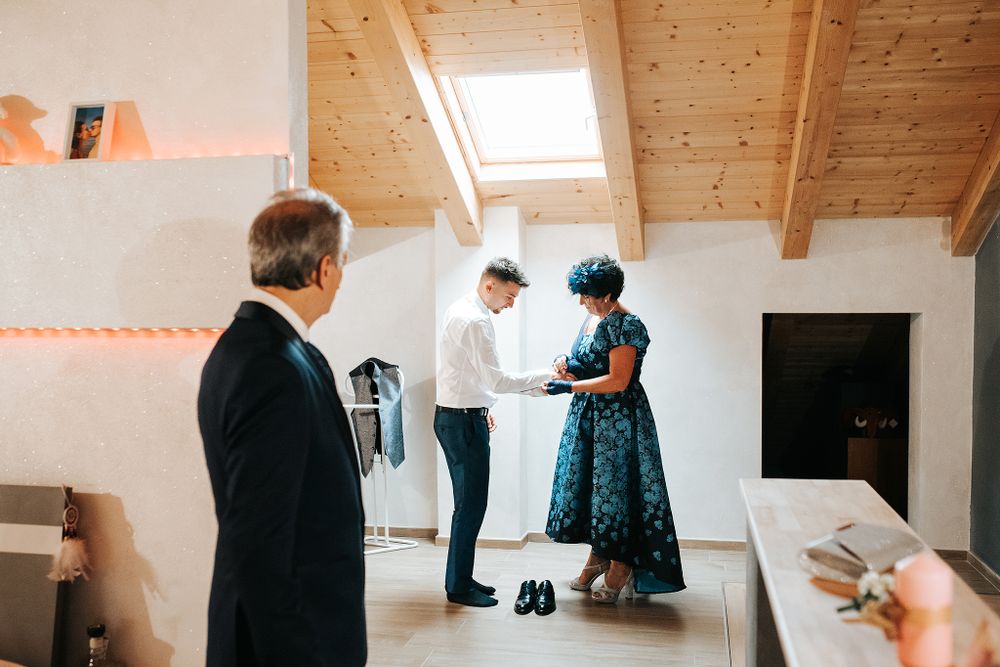 Groom getting dressed with family assistance in bright modern attic room before wedding ceremony.