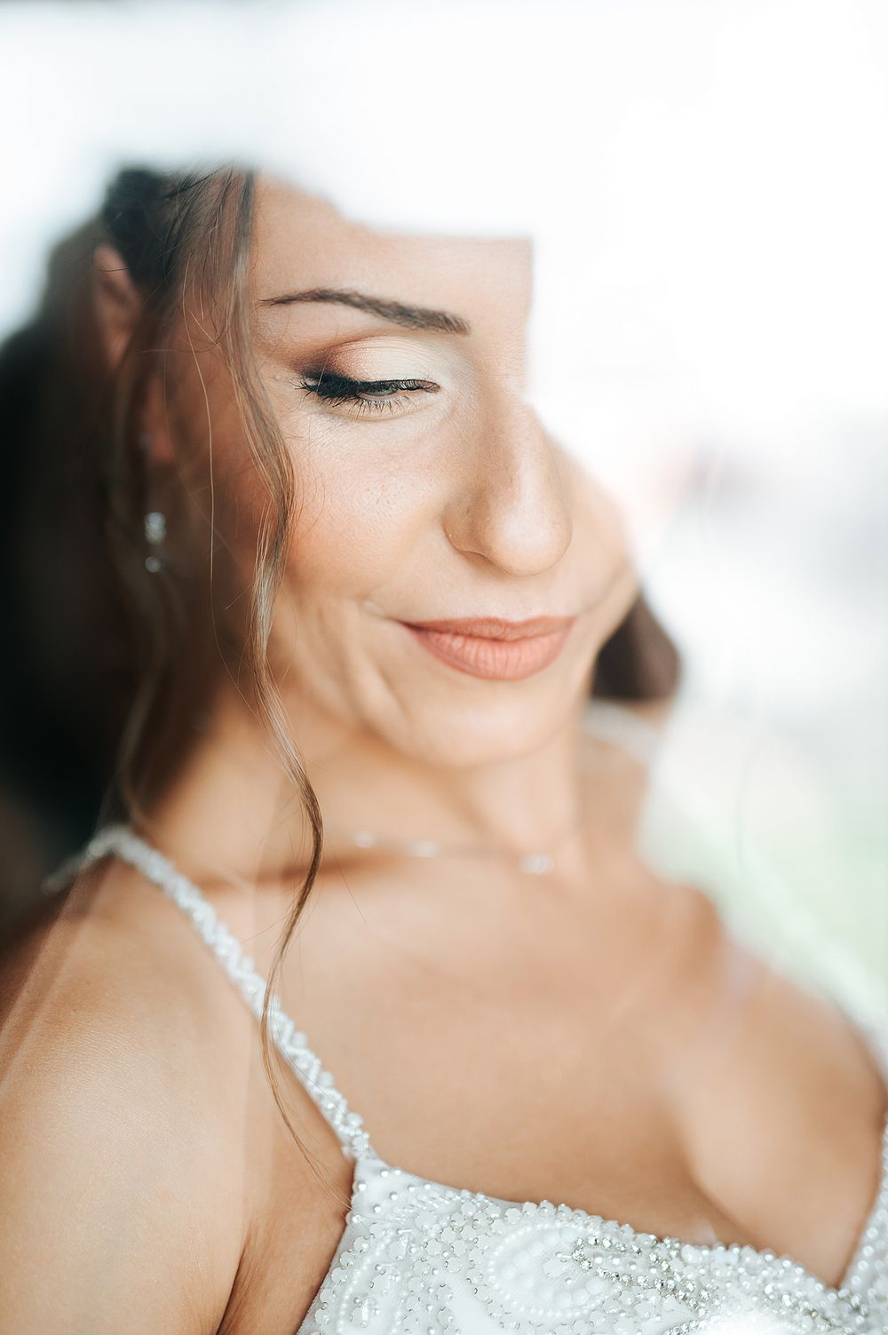 Beautiful bride smiling softly in beaded white gown with elegant makeup and drop earrings.
