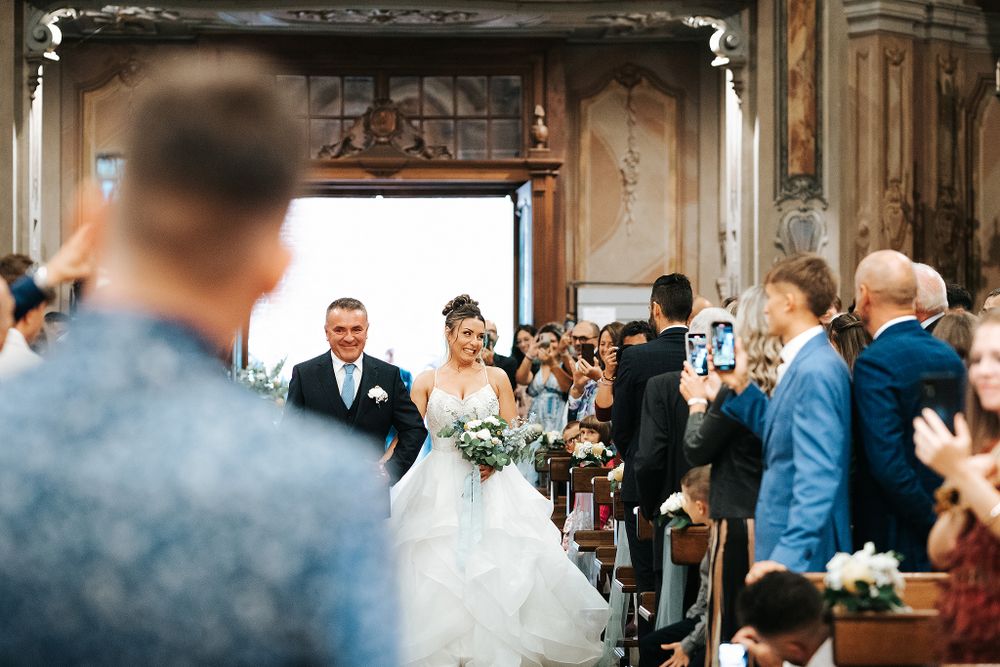 Newlyweds walking down church aisle smiling as guests applaud and photograph the happy couple.