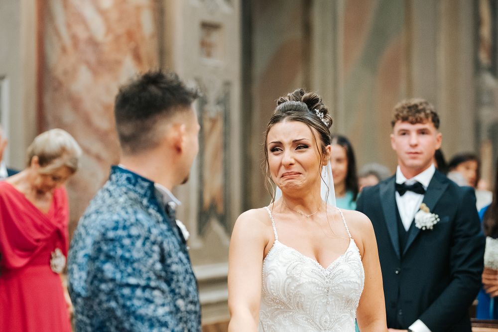 Emotional bride in beaded gown crying tears of joy during wedding ceremony at altar.