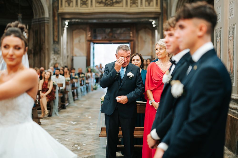 Emotional father wipes tears watching bride walk down the aisle in ornate church wedding ceremony.
