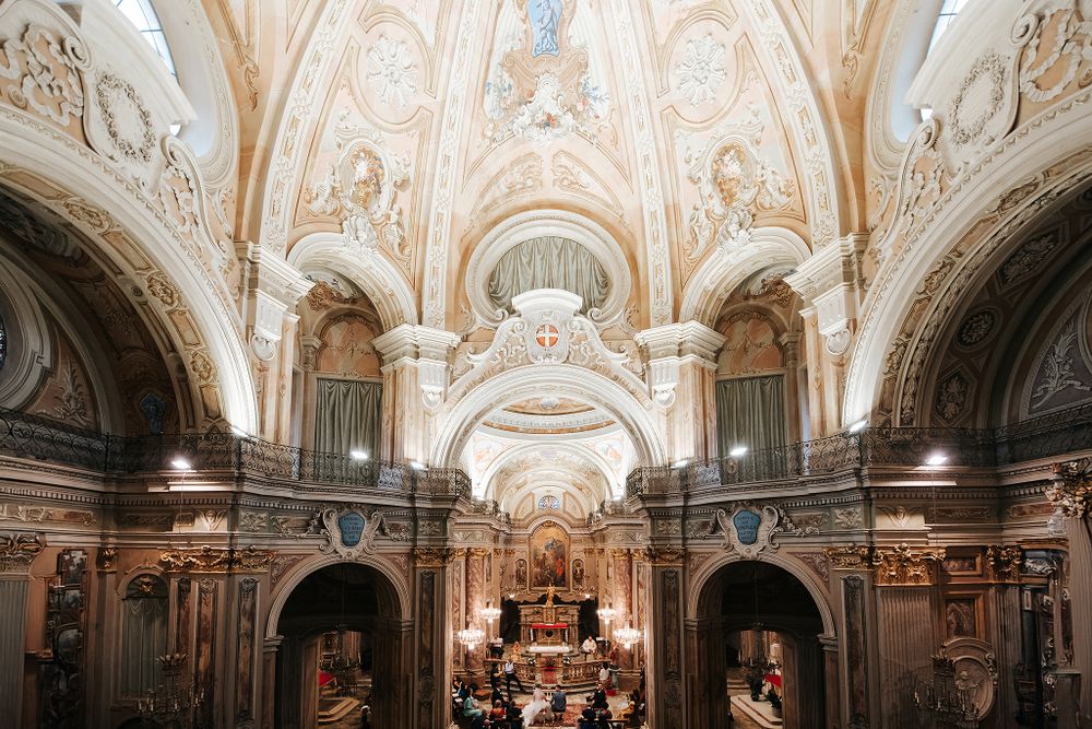 Stunning baroque church interior with ornate frescoed ceiling and altar during wedding ceremony.