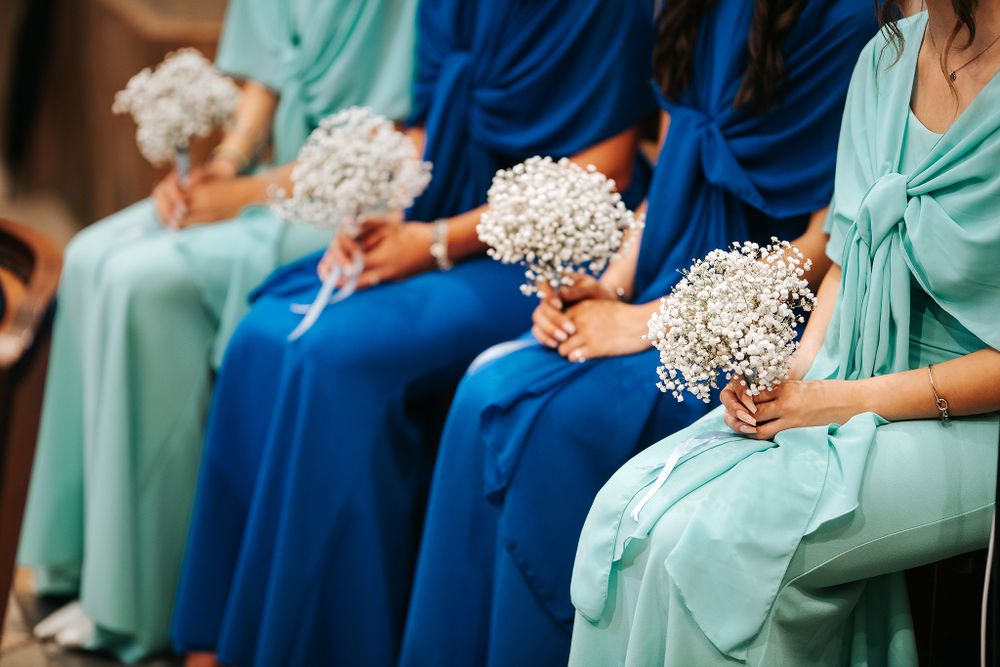 Bridesmaids in blue and teal gowns holding white baby's breath bouquets at wedding ceremony.
