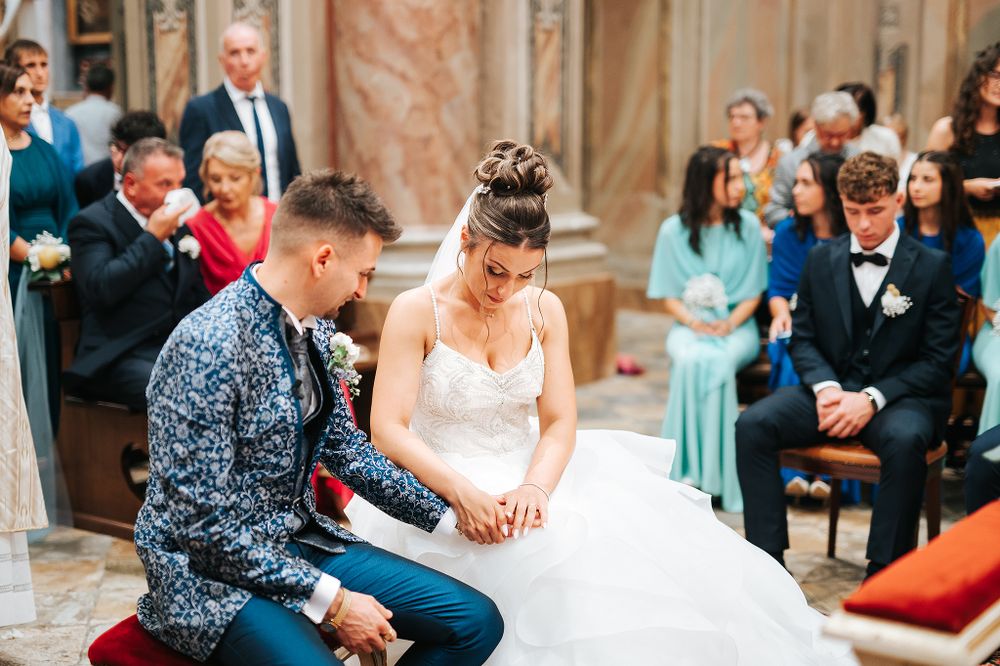 Bride and groom kneel together in prayer during traditional Catholic wedding ceremony in church.