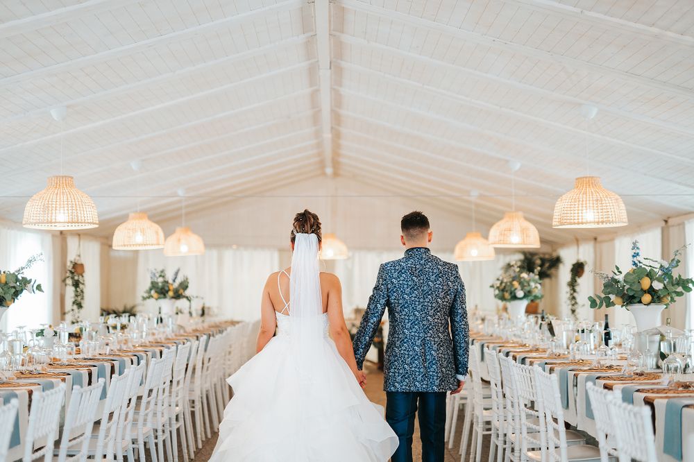 Bride and groom walk hand in hand into an elegant decorated wedding reception marquee with pendant lights.