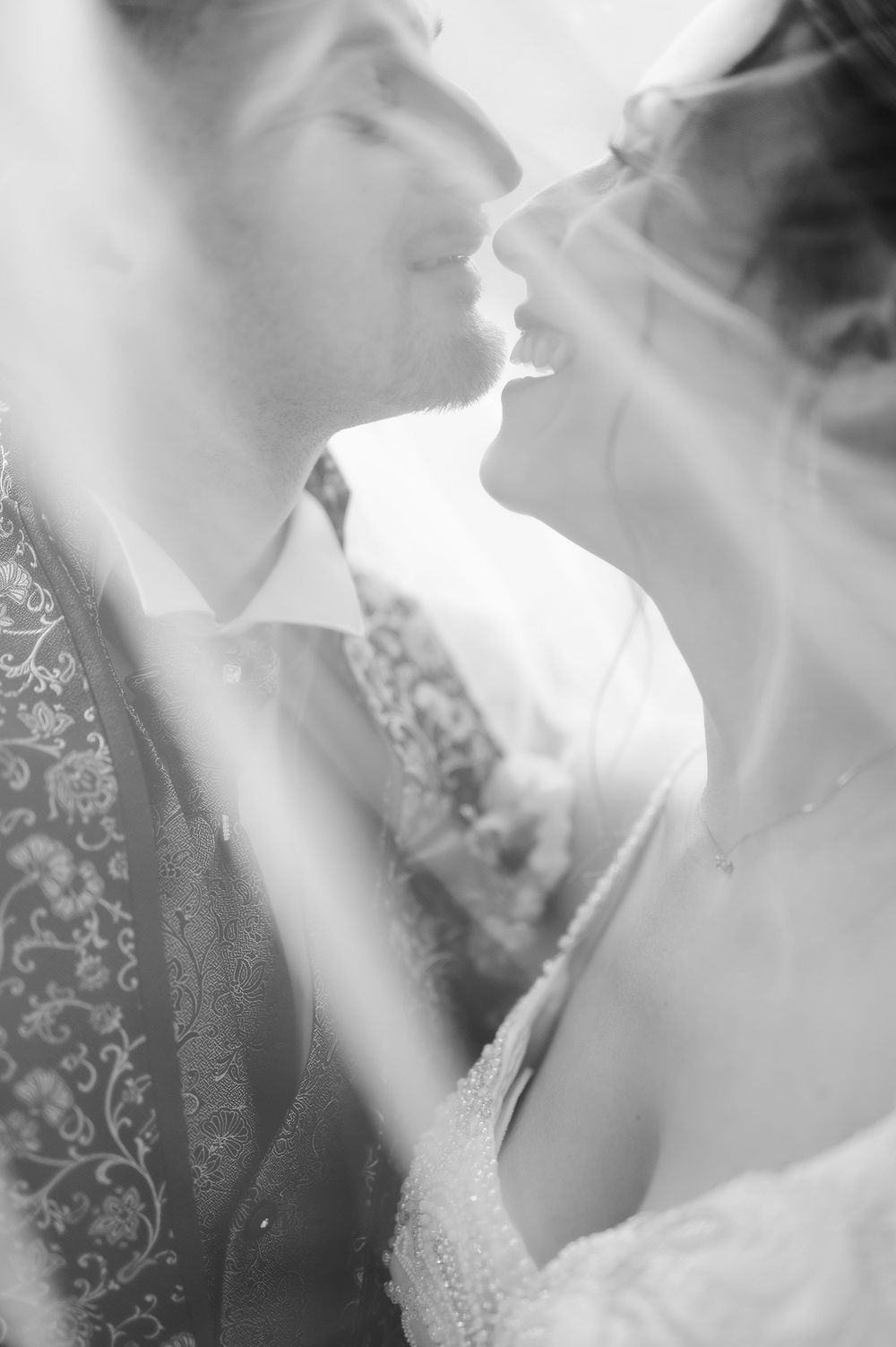 Romantic black and white photo of bride and groom almost kissing beneath a flowing wedding veil.