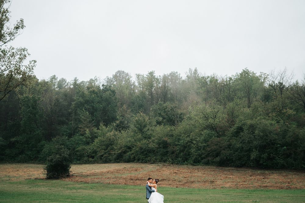 Bride and groom embrace in a wide open green field surrounded by lush trees on their wedding day.