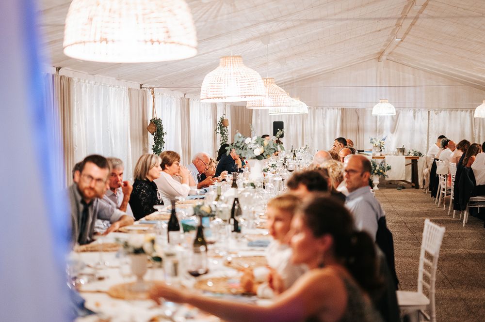 Elegant wedding reception dinner under a white marquee tent with guests seated at long tables.