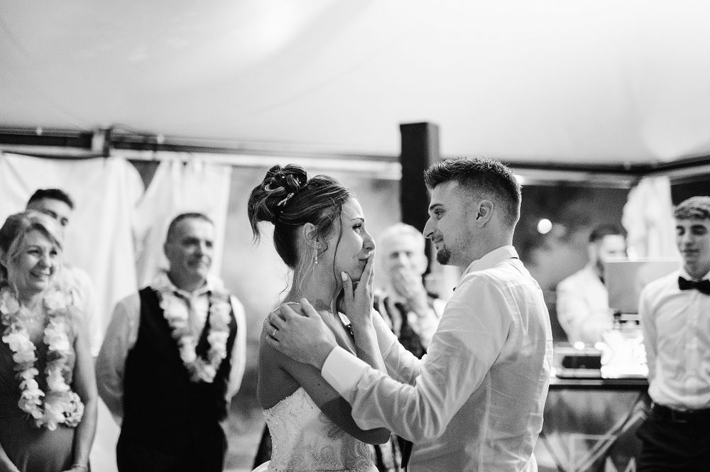 Black and white photo of bride and groom sharing first dance with guests watching at reception.