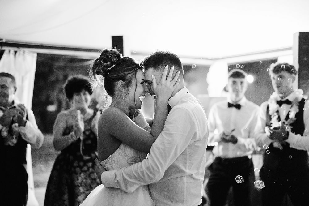 Black and white photo of bride and groom kissing during first dance with bubbles and guests.