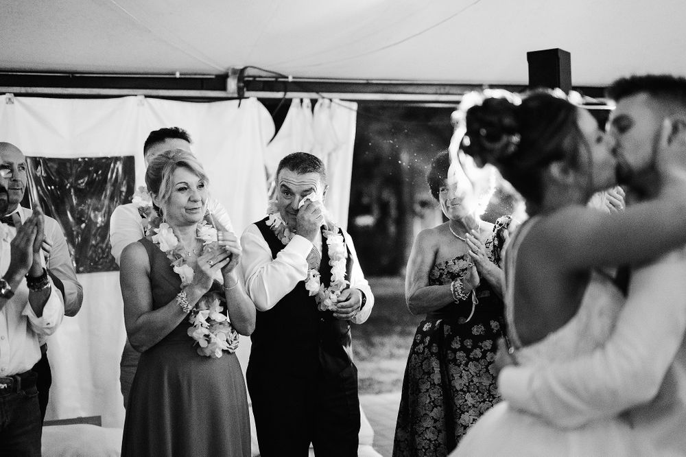 Black and white photo of wedding guests celebrating with sparklers as bride and groom kiss.