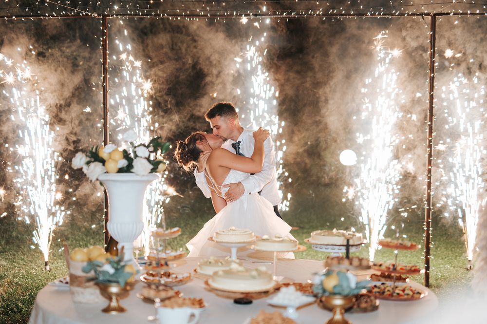 Bride and groom share romantic kiss surrounded by fountain fireworks at wedding reception.