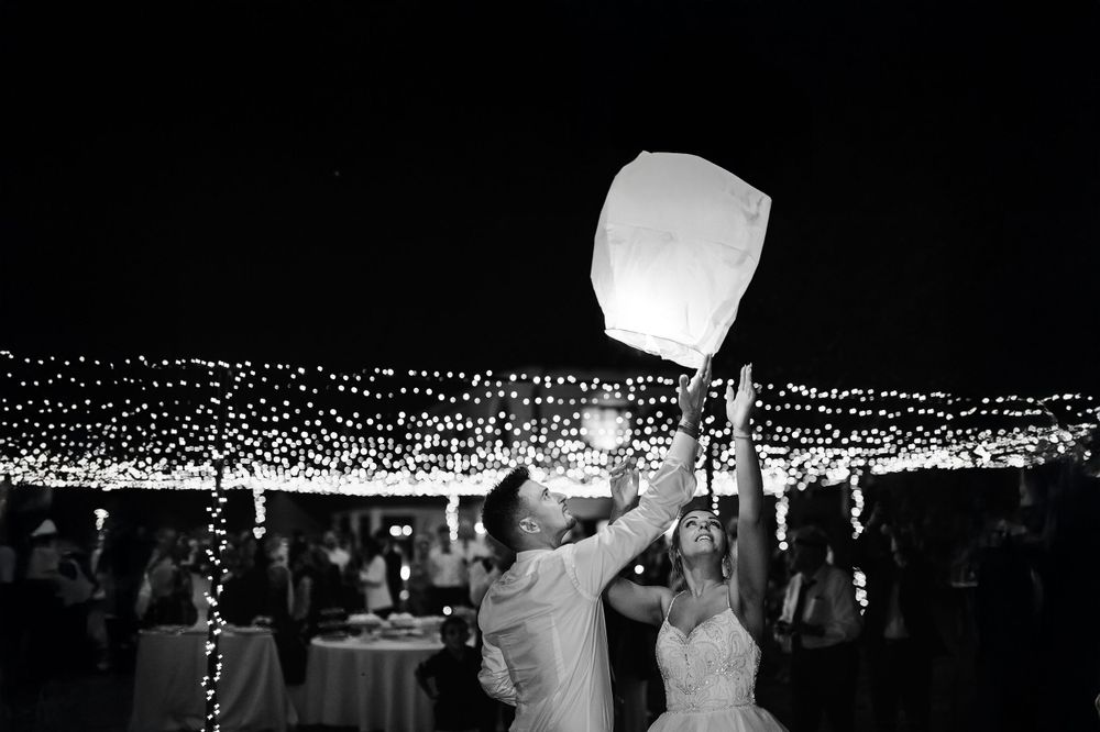 Bride and groom releasing a glowing sky lantern at their fairy light wedding reception.
