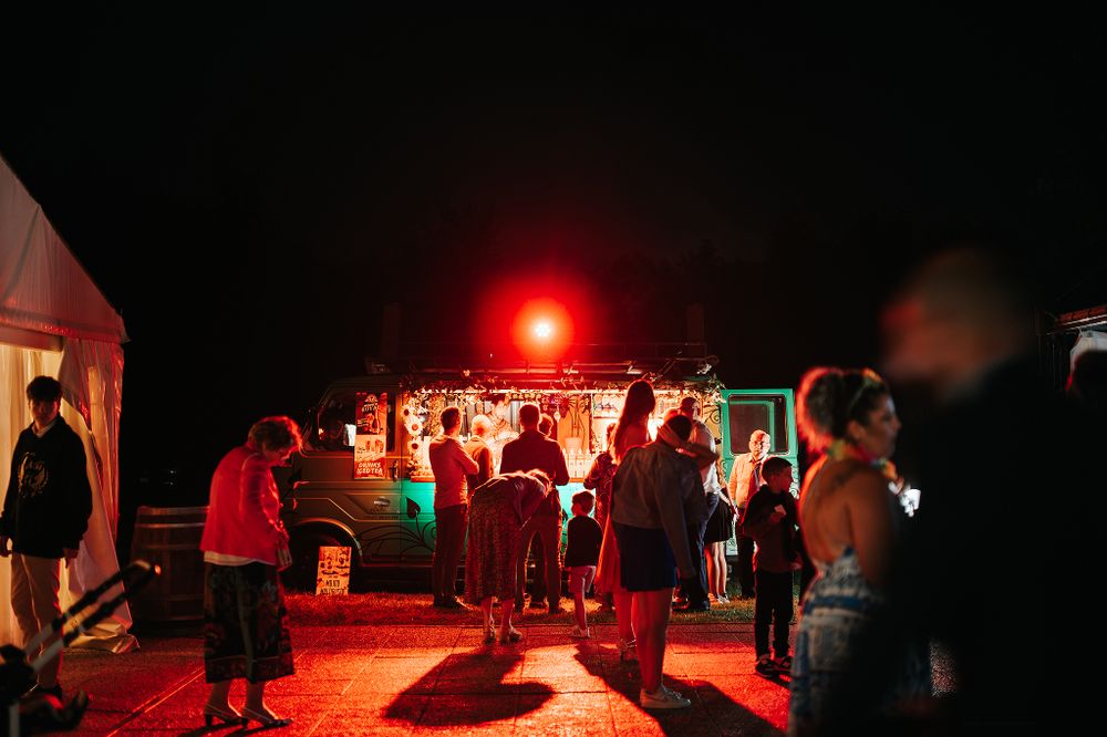 Wedding guests gathered around illuminated food truck at nighttime outdoor reception.