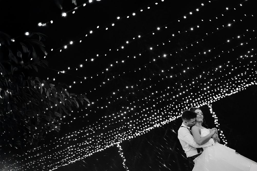 Bride and groom sharing first dance under canopy of fairy lights in black and white.