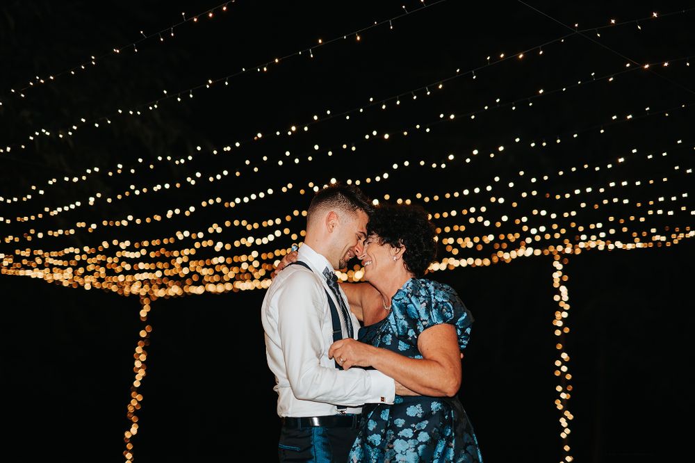 Couple sharing a tender moment under bokeh string lights at evening wedding reception.