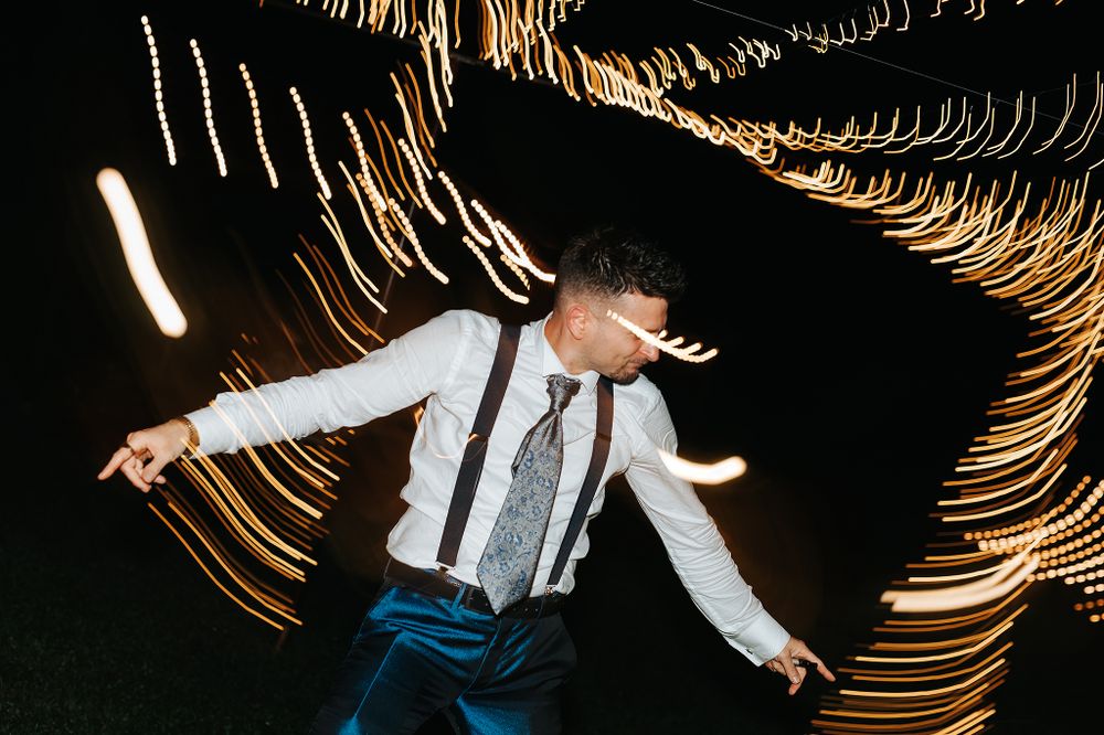 Groom dancing energetically with light trails swirling around him at wedding reception.