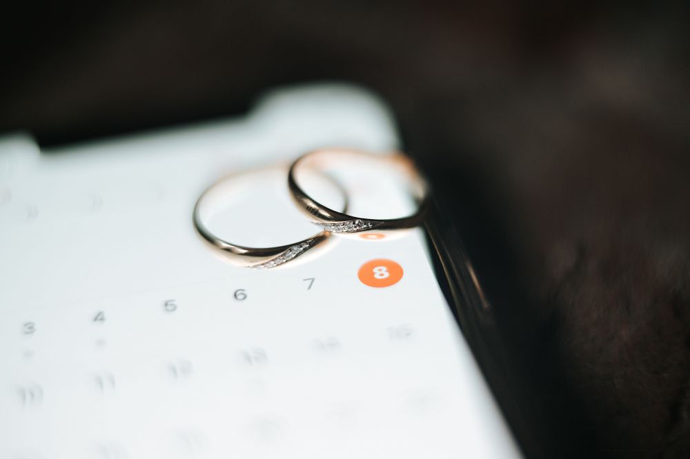 Two gold wedding bands placed on a smartphone calendar showing a circled date eight.