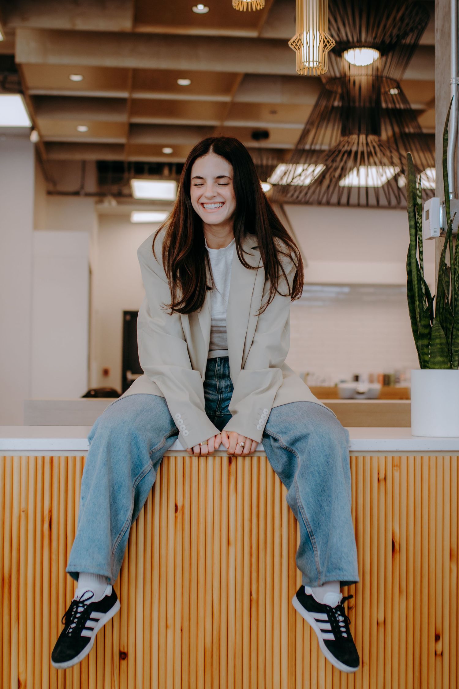Person in casual attire sitting on wooden bench under pendant lighting.