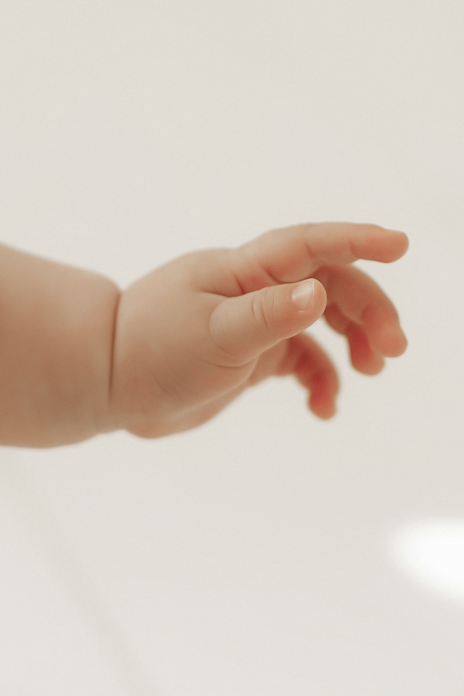 Close-up view of a small baby's hand reaching out against a soft white background.