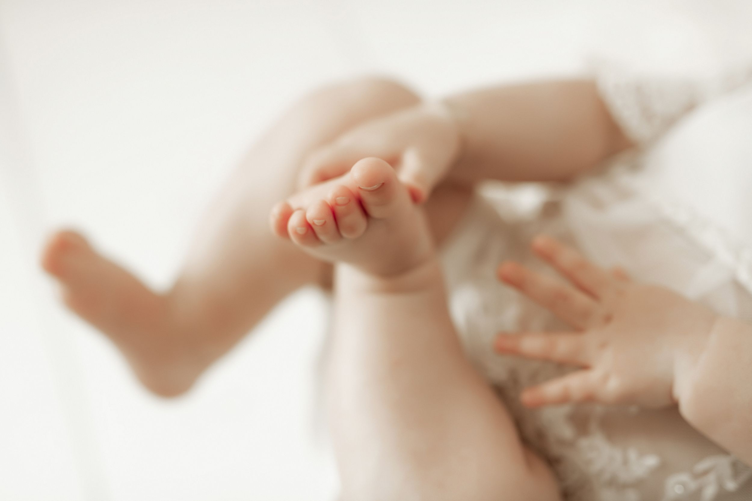 Close-up view of tiny baby feet and hands against soft white fabric in gentle lighting.