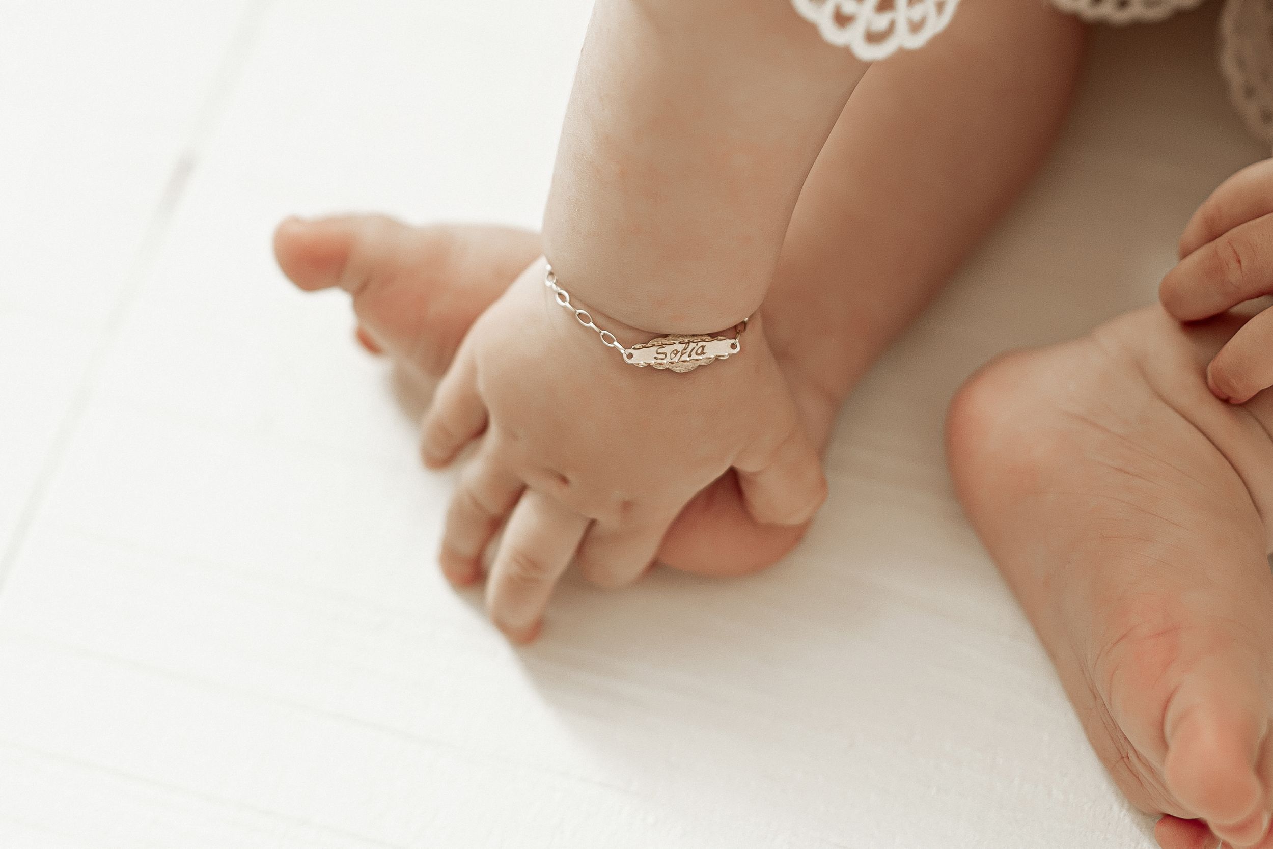 Baby's small hand and feet wearing a delicate silver anklet against a white background.