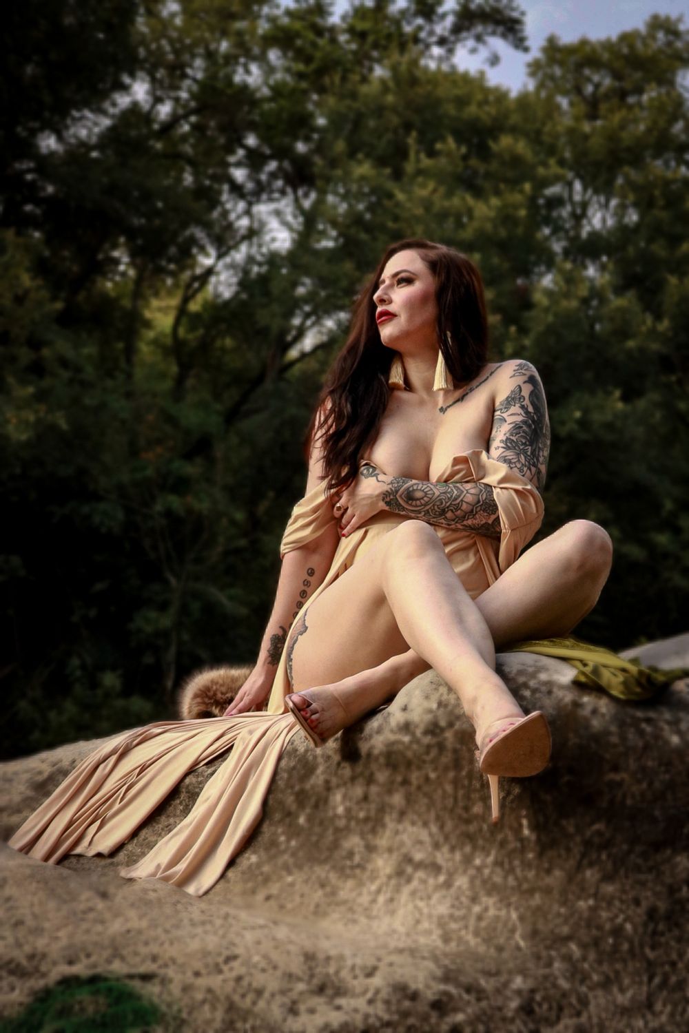 An artistic outdoor boudoir portrait of a model wearing a fringed dress while sitting on a boulder.