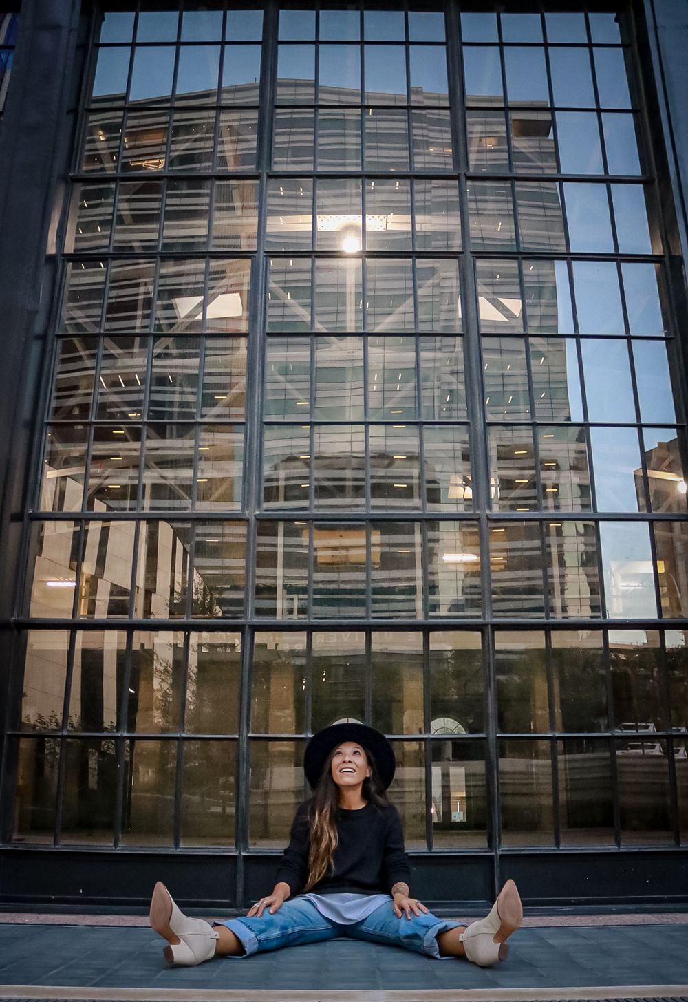 A relaxed pose in front of a modern glass building wearing a black hat and denim.