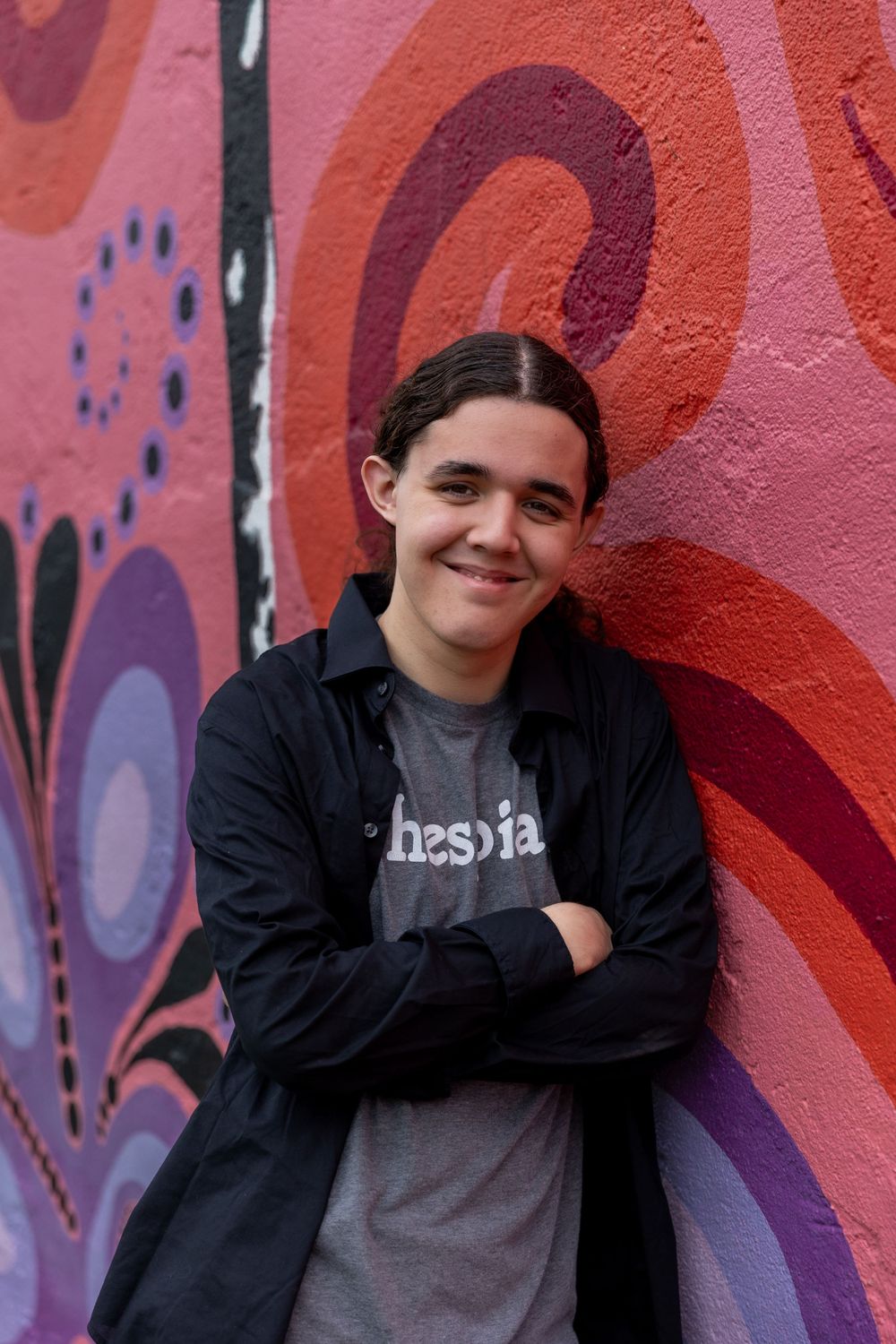 Street style senior portrait against colorful graffiti wall wearing dark jacket.