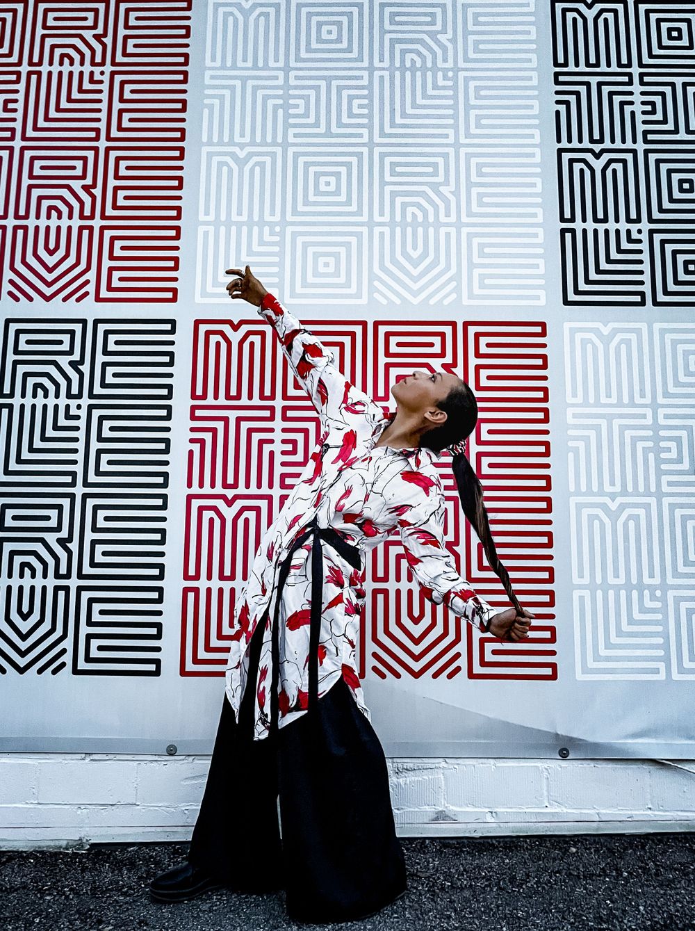 A dramatic pose against a geometric patterned wall featuring 'MORE' text in red, black and white.