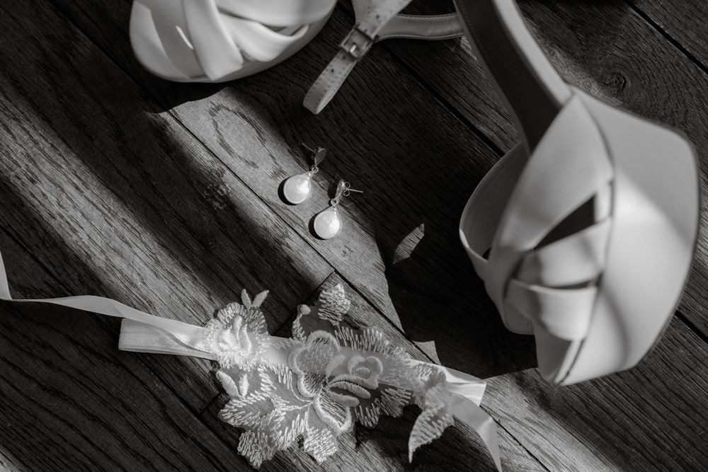 Black and white detail shot of wedding rings and lace on wooden surface.