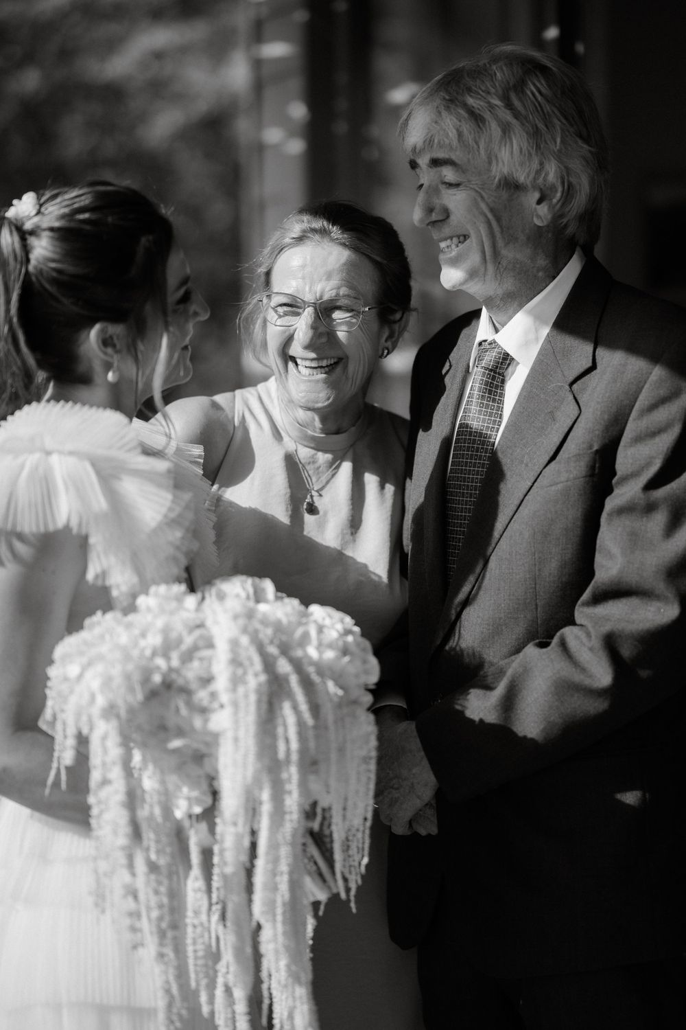 A joyful moment at a wedding as a bride shows her cascading white bouquet to smiling guests.