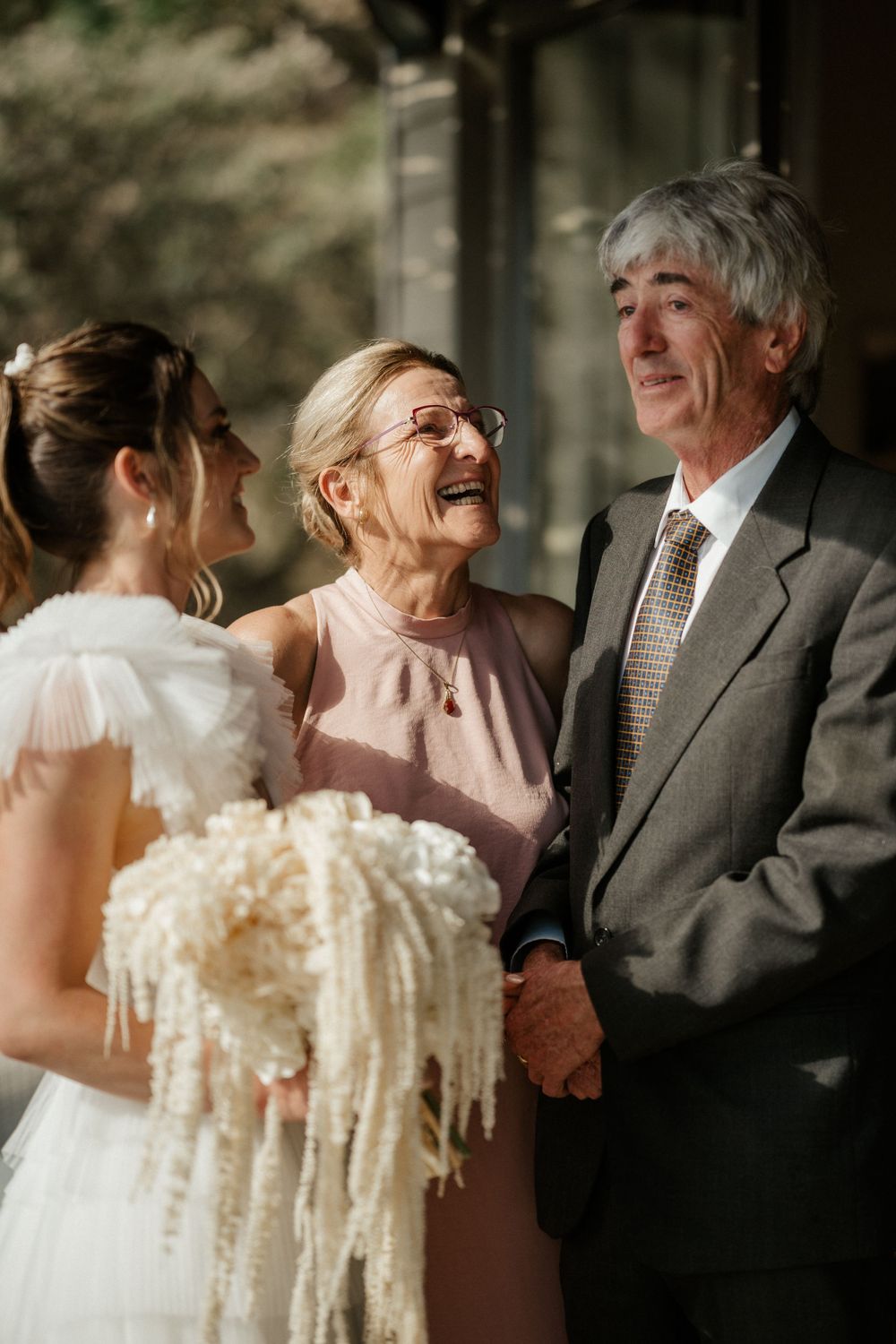 An emotional moment at a wedding as family members share joyful laughter with the bride holding a cream-colored bouquet.