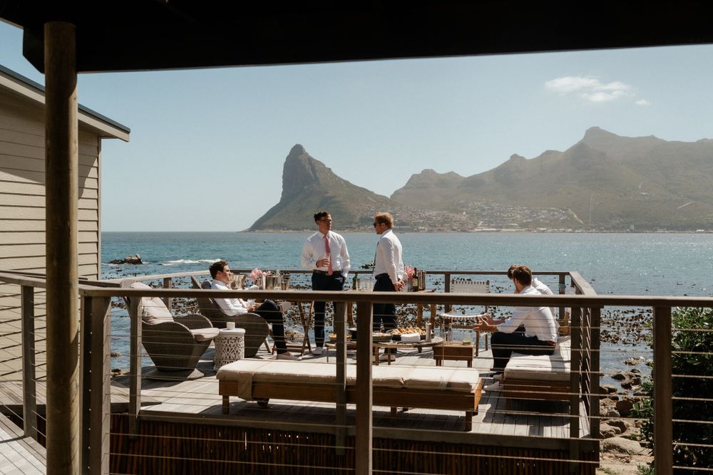 People enjoying a scenic oceanfront deck with comfortable seating and dramatic mountain views in Cape Town, South Africa.