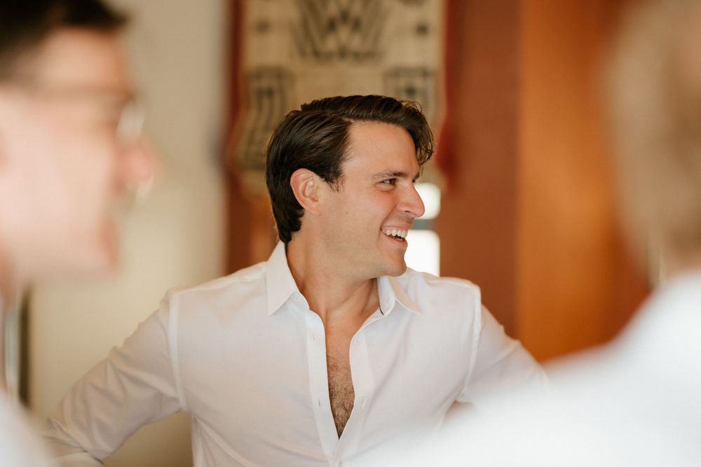Man wearing white button down shirt smiles during indoor gathering.