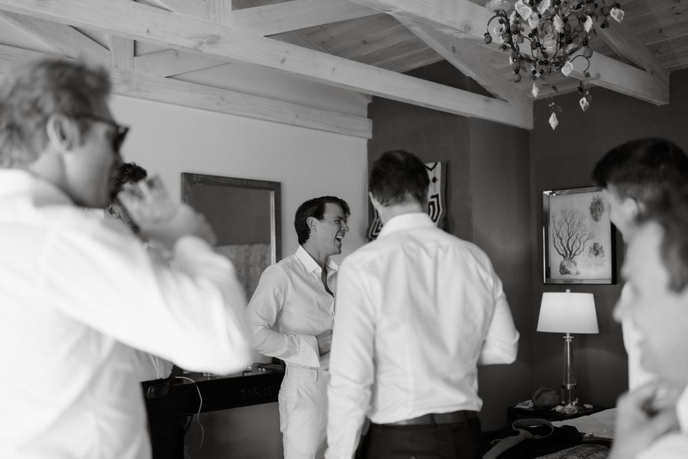 A black and white photo of groomsmen getting ready in a room with a chandelier.