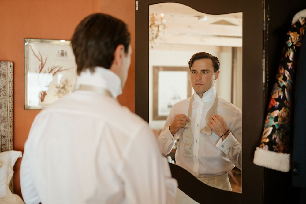 A person wearing a white button-down shirt adjusts their outfit while looking in a mirror.