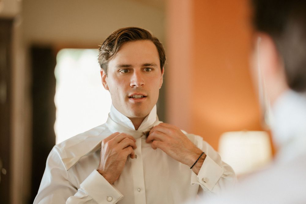 A person adjusts their bowtie in a warm-toned room while getting ready.