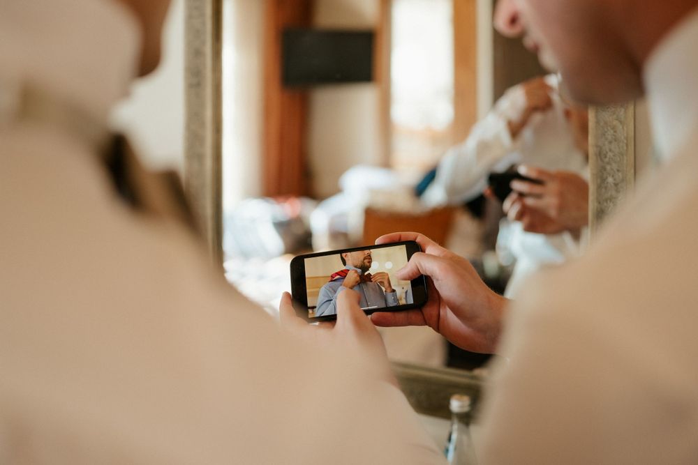 Close-up reflection in mirror of hands holding smartphone during wedding preparation.