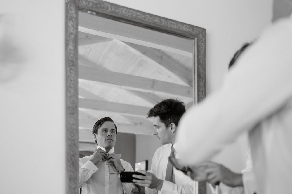 A black and white photo showing a pre-wedding preparation scene with a necktie being adjusted in a mirror.