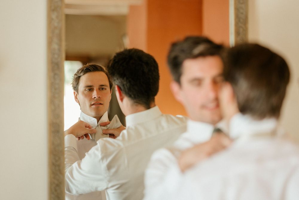 Someone in a white dress shirt adjusts their tie while looking in a mirror with reflections visible.