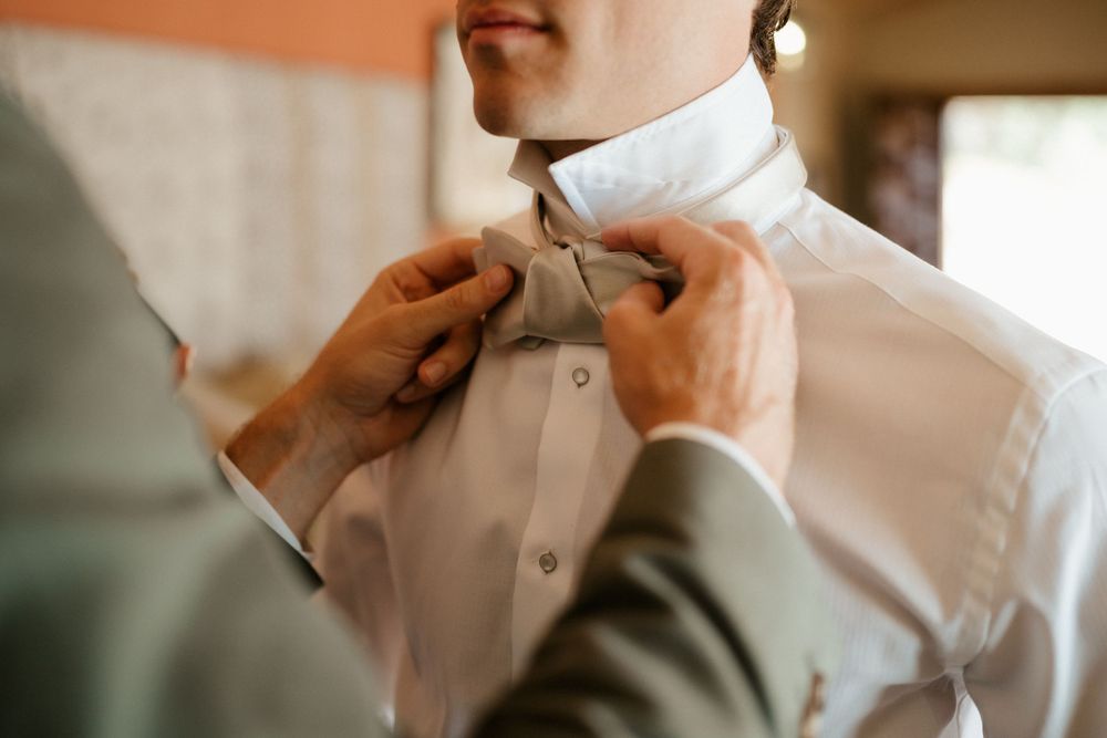 Close-up shot of hands adjusting a white bow tie on formal attire during wedding preparations.