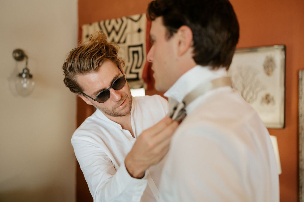 Two people getting ready in formal attire as one helps adjust the other's tie.