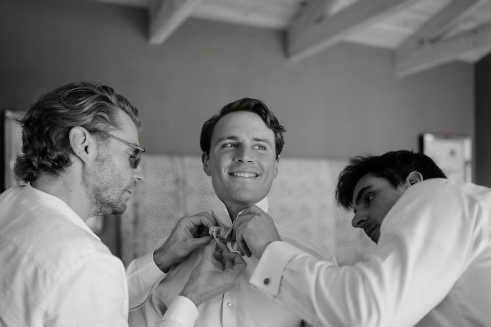 Wedding party members helping fix a bow tie in black and white photograph.