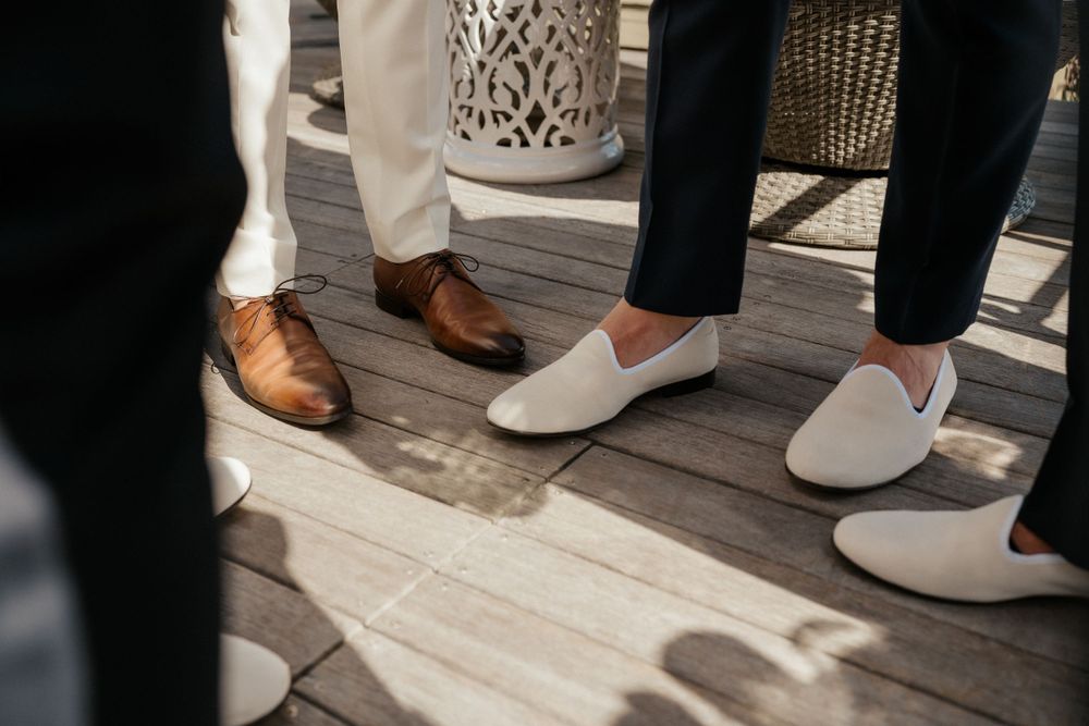 Wedding party footwear showing brown leather shoes and white loafers on wooden deck.