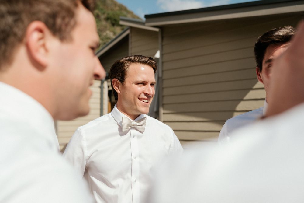 Three groomsmen share a candid laughing moment while getting ready outdoors.
