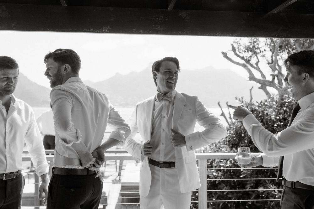 A group of people in white dress shirts stand having a conversation on a covered patio in black and white.