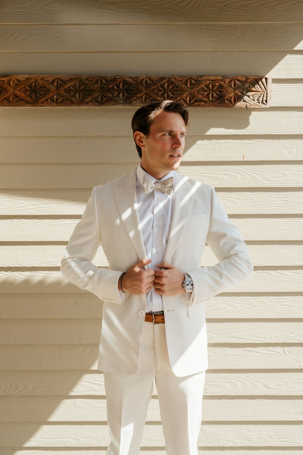 Person in crisp white suit adjusting their jacket against wooden paneled wall.